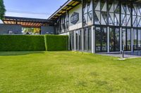 the glass walled patio and garden area has outdoor furniture on top of it with green hedges