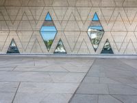 a concrete wall with triangles reflected in the windows of it and on one side a tiled floor