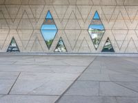 a concrete wall with triangles reflected in the windows of it and on one side a tiled floor