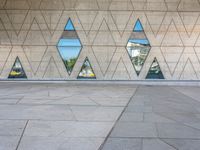 a concrete wall with triangles reflected in the windows of it and on one side a tiled floor