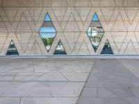 a concrete wall with triangles reflected in the windows of it and on one side a tiled floor