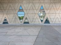 a concrete wall with triangles reflected in the windows of it and on one side a tiled floor