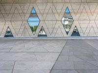 a concrete wall with triangles reflected in the windows of it and on one side a tiled floor