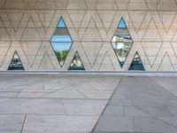 a concrete wall with triangles reflected in the windows of it and on one side a tiled floor