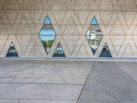 a concrete wall with triangles reflected in the windows of it and on one side a tiled floor