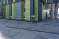 a bicycle locked to a post and in front of a green glass building with columns