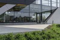 the rear of an office building with plants in front of it and a clock at the entrance