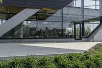 the rear of an office building with plants in front of it and a clock at the entrance