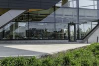 the rear of an office building with plants in front of it and a clock at the entrance