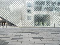 a building that is covered with large glass walls near some trees and cars parked on the sidewalk