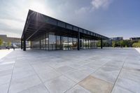 a glass covered building sits alone in a square park area with sunlight shining in the background