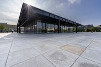 a glass covered building sits alone in a square park area with sunlight shining in the background