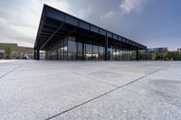 a glass covered building sits alone in a square park area with sunlight shining in the background