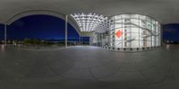 a fisheye view of the outside of a building at night time, of an orange kite flying over