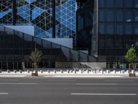 an empty road in front of a tall building with geometric glass windows and plants in the ground