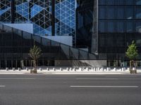 an empty road in front of a tall building with geometric glass windows and plants in the ground