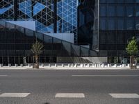 an empty road in front of a tall building with geometric glass windows and plants in the ground