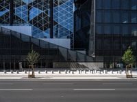 an empty road in front of a tall building with geometric glass windows and plants in the ground