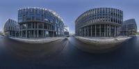 a fish eye image of a glassy building in the middle of a street, with some people on one side of it