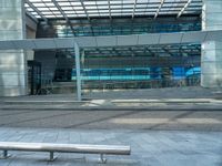 a bench sitting outside of a glassy building next to a staircase next to an entrance