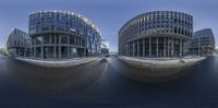 a fish eye image of a glassy building in the middle of a street, with some people on one side of it