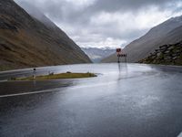 an empty roadway with a mountain side road running alongside it in the distance is water and some rocks