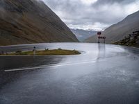 an empty roadway with a mountain side road running alongside it in the distance is water and some rocks