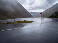 an empty roadway with a mountain side road running alongside it in the distance is water and some rocks