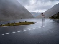 an empty roadway with a mountain side road running alongside it in the distance is water and some rocks