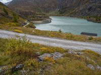 a dirt road next to the water and mountains with a lake and a mountain in the background