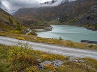 a dirt road next to the water and mountains with a lake and a mountain in the background