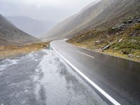 two sheep are standing by a curved road in the mountainside while cloudy skies gather overhead