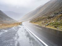 two sheep are standing by a curved road in the mountainside while cloudy skies gather overhead