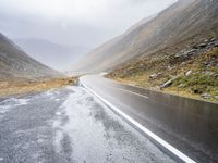 two sheep are standing by a curved road in the mountainside while cloudy skies gather overhead