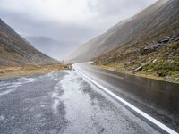 two sheep are standing by a curved road in the mountainside while cloudy skies gather overhead