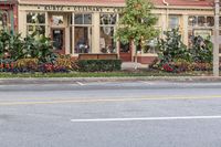 a man riding a motorcycle down a street next to a business building with flowers on each side