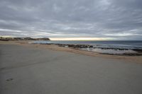 a man walking on the beach towards the ocean in an open space on a cloudy day