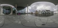 the 360 - fisheye lens is pointed at the circular building's exterior as well as a person riding an orange bike