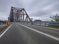 the bridge has a long metal structure with two cars on it on a cloudy day