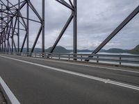 an empty road next to the water on a bridge during the day or evening with clouds overhead