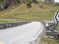 a curved road with stone barriers and an umbrella on the side of the road near rocks and grass