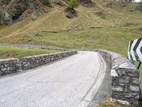 a curved road with stone barriers and an umbrella on the side of the road near rocks and grass