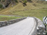 a curved road with stone barriers and an umbrella on the side of the road near rocks and grass