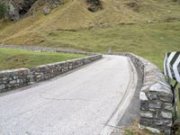 a curved road with stone barriers and an umbrella on the side of the road near rocks and grass