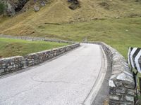 a curved road with stone barriers and an umbrella on the side of the road near rocks and grass