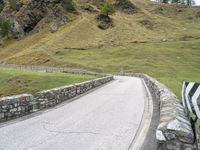 a curved road with stone barriers and an umbrella on the side of the road near rocks and grass