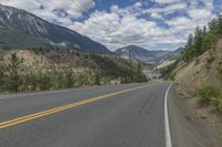 a large road with two yellow stripes in the middle of it surrounded by trees and mountains