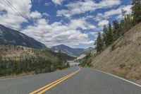 a large road with two yellow stripes in the middle of it surrounded by trees and mountains