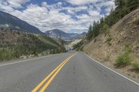 a large road with two yellow stripes in the middle of it surrounded by trees and mountains