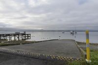 a dock with boats is empty and the water near it is very calm, with a few boats on the water